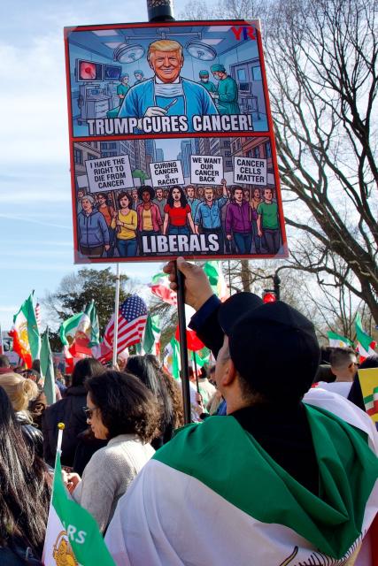 A protester holds a sign reading "Trump cures cancer" as they march toward the White House during a rally in support of Iranians' fight for freedom, in Washington, DC, on March 29, 2026. The event, organized by DCProtests4Iran, brought together members of the Iranian diaspora from the Washington, DC metropolitan area and surrounding states. (Photo by Amid FARAHI / AFP)