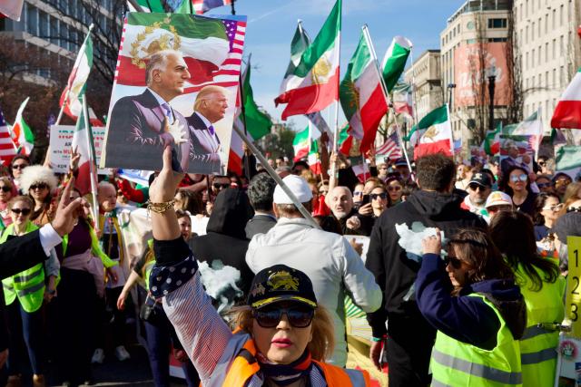 A woman holds up a sign featuring an image of Reza Pahlavi, son of the last shah of Iran, and US President Donald Trump as demonstrators march toward the White House during a rally in support of Iranians' fight for freedom, in Washington, DC, on March 29, 2026. The event, organized by DCProtests4Iran, brought together members of the Iranian diaspora from the Washington, DC metropolitan area and surrounding states. (Photo by Amid FARAHI / AFP)