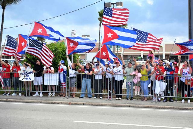 People wave Cuban and US flags as the motorcade of US President Donald Trump passes by on its way to Palm Beach International Airport in West Palm Beach, Florida, March 29, 2026. US President Donald Trump is returning to the White House after spending the weekend at his Mar-a-Lago residence. (Photo by Mandel NGAN / AFP)