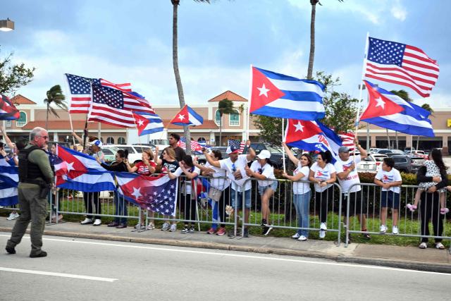People wave Cuban and US flags as the motorcade of US President Donald Trump passes by on its way to Palm Beach International Airport in West Palm Beach, Florida, March 29, 2026. US President Donald Trump is returning to the White House after spending the weekend at his Mar-a-Lago residence. (Photo by Mandel NGAN / AFP)