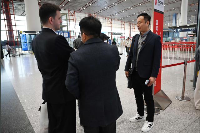 Zhao Bin, a Chinese business traveller (R), speaks to media after checking in for a flight to Pyongyang, North Korea, at Beijing airport on March 30, 2026. Air China restarted direct flights between Beijing and Pyongyang on Marach 30 after a six-year hiatus, another sign isolated North Korea is gradually opening up following the resumption of train services between the capitals. (Photo by GREG BAKER / AFP)