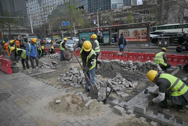 Workers rebuild a sidewalk in Beijing on March 30, 2026. (Photo by Pedro PARDO / AFP)