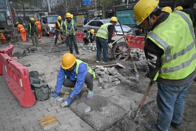 Workers rebuild a sidewalk in Beijing on March 30, 2026. (Photo by Pedro PARDO / AFP)