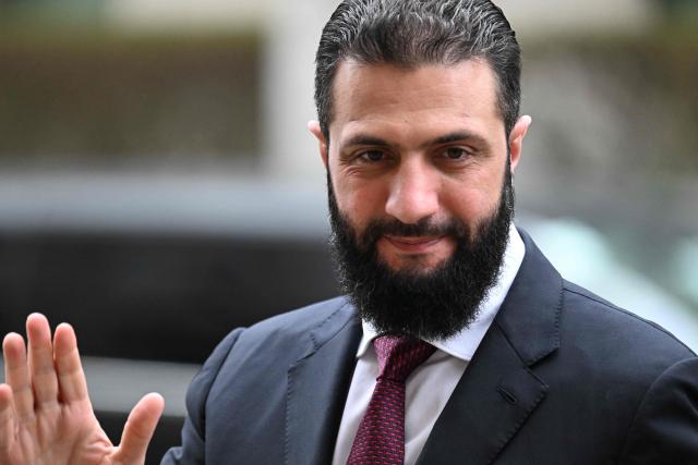 Syrian President Ahmed al-Sharaa waves as he arrives ahead a German-Syrian roundtable meeting on economy at the Foreign Ministry in Berlin on March 30, 2026. Syria's President Ahmed al-Sharaa visits Germany on Monday for talks on the Middle East war, rebuilding his country and Berlin's efforts to send back Syrian refugees. (Photo by RALF HIRSCHBERGER / AFP)