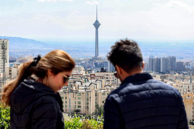 A couple stands at a park in northern Tehran overlooking the Iranian capital's skyline with Milad (Birth) Tower, the tallest tower in the country at 435 metres, pictured in the background, on March 30, 2026. Israel and Iran exchanged more missile fire on March 30 as concerns that the US might escalate the Middle East conflict by launching ground raids against the Islamic republic's Gulf islands sent oil prices soaring. (Photo by AFP) / 