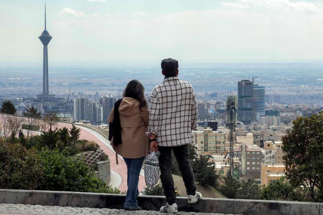 A couple stands at a park in northern Tehran overlooking the Iranian capital's skyline with Milad (Birth) Tower, the tallest tower in the country at 435 metres, pictured in the background, on March 30, 2026. Israel and Iran exchanged more missile fire on March 30 as concerns that the US might escalate the Middle East conflict by launching ground raids against the Islamic republic's Gulf islands sent oil prices soaring. (Photo by AFP) / 