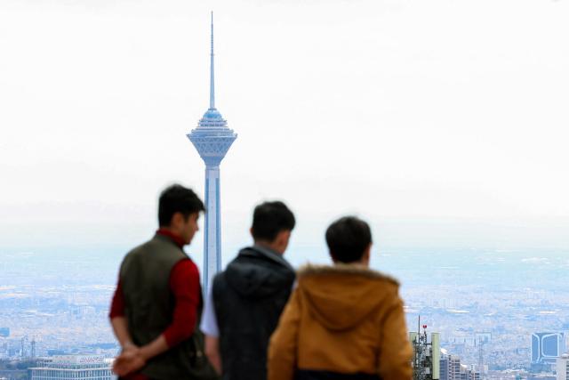 Milad (Birth) Tower, the tallest tower in Iran at 435 metres, is pictured behind people standing at a park in northern Tehran overlooking the Iranian capital on March 30, 2026. Israel and Iran exchanged more missile fire on March 30 as concerns that the US might escalate the Middle East conflict by launching ground raids against the Islamic republic's Gulf islands sent oil prices soaring. (Photo by AFP) / 