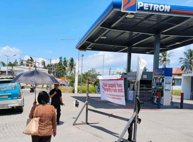 Pedestrians walk past a sign at a petrol station in Tacloban City, Leyte province, central Philippines on March 30, 2026. The Philippines' sole oil refinery has secured nearly 2.5 million barrels of Russian crude out of "extreme necessity", a stock exchange filing revealed on March 30, as the country seeks to replenish fast-dwindling fuel reserves. (Photo by Marlon TANO / AFP)