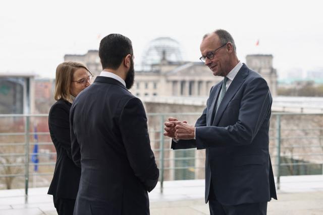 German Chancellor Friedrich Merz speaks with Syrian President Ahmed al-Sharaa on the terrace of the Chancellery, with the Reichstag building in the background, ahead of their bilateral talks on March 30, 2026 in Berlin. Syria's President Ahmed al-Sharaa visits Germany on Monday for talks on the Middle East war, rebuilding his country and Berlin's efforts to send back Syrian refugees. (Photo by Nadja Wohlleben / POOL / AFP)