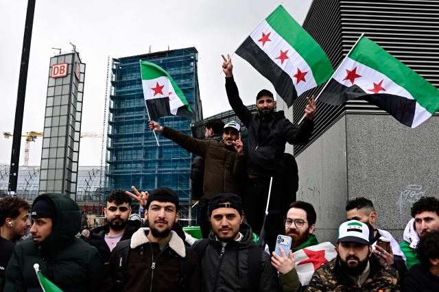 Demonstrators raise the flag of Syria during a demostration in front of the main train station in Berlin on March 30, 2026. Syria's President Ahmed al-Sharaa visits Germany on March 30, 2026 for talks on the Middle East war, rebuilding his country and Berlin's efforts to send back Syrian refugees. (Photo by Tobias SCHWARZ / AFP)
