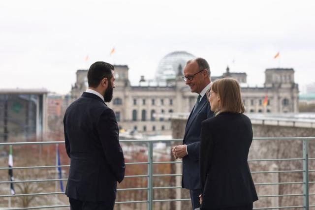 German Chancellor Friedrich Merz speaks with Syrian President Ahmed al-Sharaa, with the help of a translator, on the terrace of the Chancellery, with the Reichstag building in the background, ahead of their bilateral talks on March 30, 2026 in Berlin. Syria's President Ahmed al-Sharaa visits Germany on Monday for talks on the Middle East war, rebuilding his country and Berlin's efforts to send back Syrian refugees. (Photo by Nadja Wohlleben / POOL / AFP)