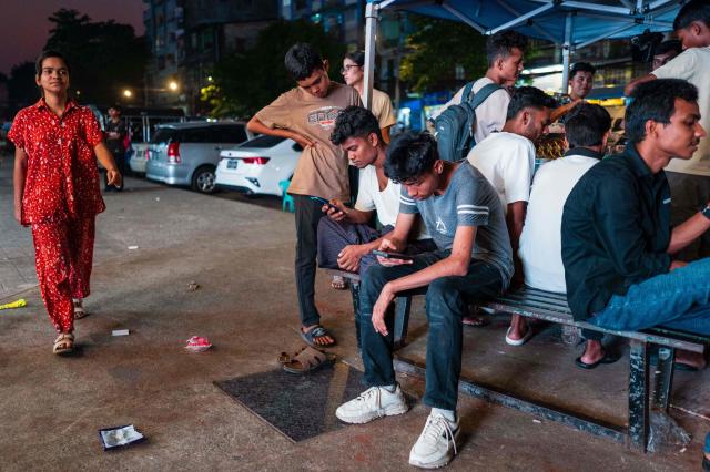 People use their mobile phones on a street in Yangon on March 29, 2026. (Photo by ANTHONY WALLACE / AFP)