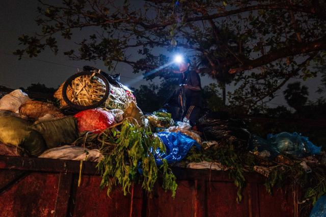 A worker with a headlight sorts through litter in a skip in Yangon on March 29, 2026. (Photo by ANTHONY WALLACE / AFP)