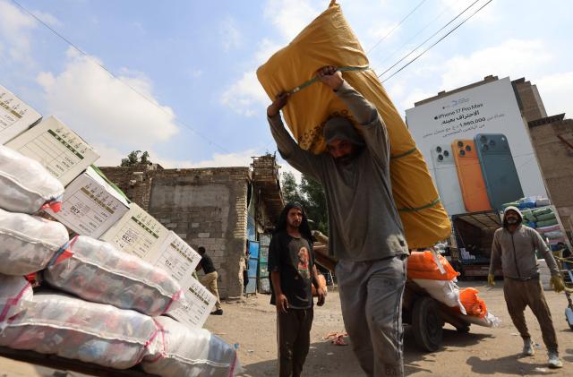 Workers load goods onto trucks at a transport garage in the Maidan area of central Baghdad on March 30, 2026. As cargo ships remain unable to enter Iraq's port of Umm Qasr along the Gulf due to the closure of the Hormuz Strait due to the war between Iran and the US and Israel, Iraq's trade has been severely impacted negatively, depending mainly now on overland transport. (Photo by AHMAD AL-RUBAYE / AFP)