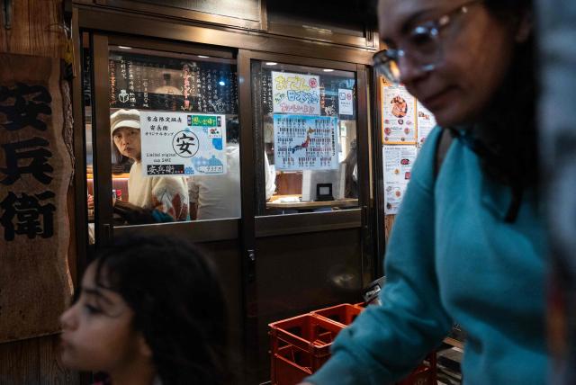 A woman looks out from a small restaurant as tourists pass through an alley in Shinjuku City, Tokyo on March 30, 2026. (Photo by Andrew CABALLERO-REYNOLDS / AFP)