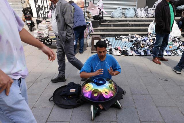 A man plays music as people walk at the Grand Bazaar in Tehran on March 30, 2026. US President Donald Trump pushed concerns about surging world prices aside on March 30 and threatened to destroy Iran's oil wells, power plants and main export terminal if Tehran does not quickly accept a peace deal. (Photo by ATTA KENARE / AFP) / 