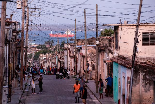 People walk trough a street, with an oil tanker ship in the background, in Matanzas, Cuba on March 30, 2026. US President Donald Trump said on March 29, 2026, that Moscow could send oil to Cuba despite Washington's de facto fuel blockade, as a Russian tanker was expected to deliver some much-needed crude to the crisis-hit island. The Anatoly Kolodkin, which is carrying 730,000 barrels of crude, was off northeast Cuba on the evening of March 29 and is expected to dock in the western port of Matanzas by March 31, according to shipping tracker MarineTraffic. (Photo by AFP)