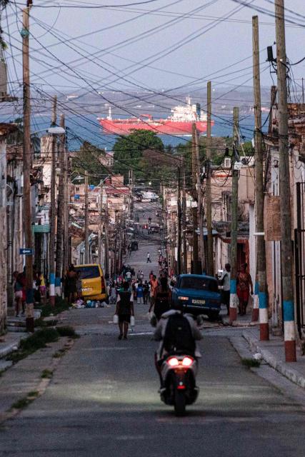 People walk trough a street, with an oil tanker ship in the background, in Matanzas, Cuba on March 30, 2026. US President Donald Trump said on March 29, 2026, that Moscow could send oil to Cuba despite Washington's de facto fuel blockade, as a Russian tanker was expected to deliver some much-needed crude to the crisis-hit island. The Anatoly Kolodkin, which is carrying 730,000 barrels of crude, was off northeast Cuba on the evening of March 29 and is expected to dock in the western port of Matanzas by March 31, according to shipping tracker MarineTraffic. (Photo by AFP)