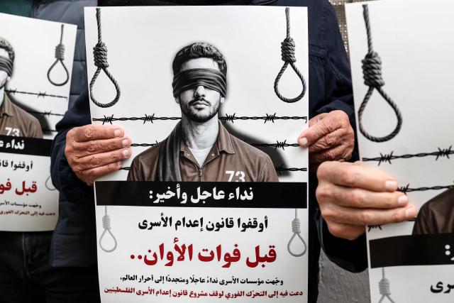 Protesters hold placards outside the Red Cross offices in Ramallah, in the Israeli-occupied West Bank, on March 31, 2026, during a rally against a bill approved by Israel's parliament that would allow the execution of Palestinians convicted on terror charges for deadly attacks. Israel's parliament approved a bill on March 30, that would allow the execution of Palestinians convicted on terror charges for deadly attacks, a move that has been criticised as discriminatory and immediately drew a court challenge. (Photo by Zain JAAFAR / AFP)