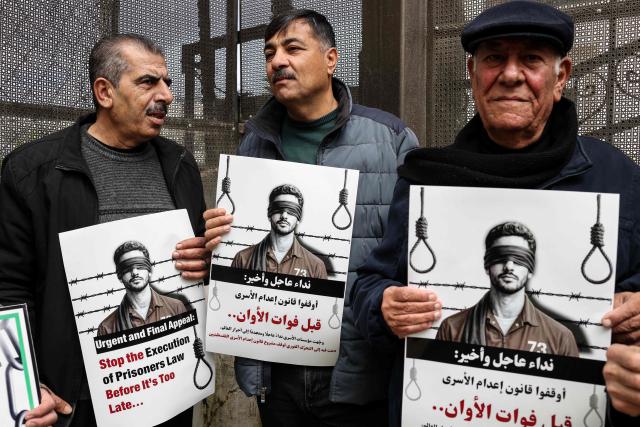 Protesters hold placards outside the Red Cross offices in Ramallah, in the Israeli-occupied West Bank, on March 31, 2026, during a rally against a bill approved by Israel's parliament that would allow the execution of Palestinians convicted on terror charges for deadly attacks. Israel's parliament approved a bill on March 30, that would allow the execution of Palestinians convicted on terror charges for deadly attacks, a move that has been criticised as discriminatory and immediately drew a court challenge. (Photo by Zain JAAFAR / AFP)