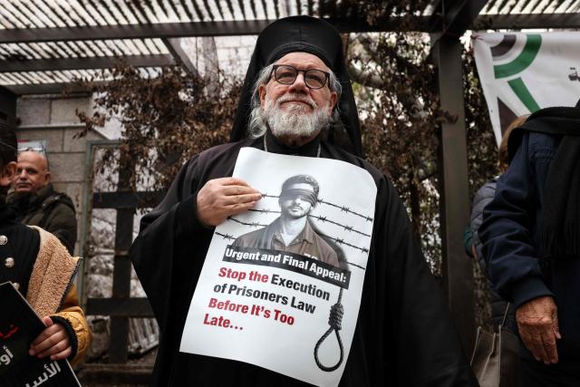 A member of the clergy holds a placard outside the Red Cross offices in Ramallah, in the Israeli-occupied West Bank, on March 31, 2026, during a rally against a bill approved by Israel's parliament that would allow the execution of Palestinians convicted on terror charges for deadly attacks. Israel's parliament approved a bill on March 30, that would allow the execution of Palestinians convicted on terror charges for deadly attacks, a move that has been criticised as discriminatory and immediately drew a court challenge. (Photo by Zain JAAFAR / AFP)