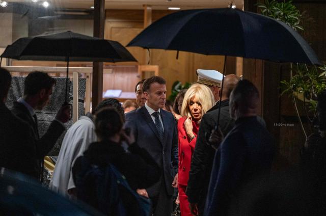 French President Emmanuel Macron (center L) and his wife Brigitte Macron (center R) leave the Ginza Motoji showroom on a rainy night in Tokyo on March 31, 2026. (Photo by ANDREW CABALLERO-REYNOLDS / AFP)