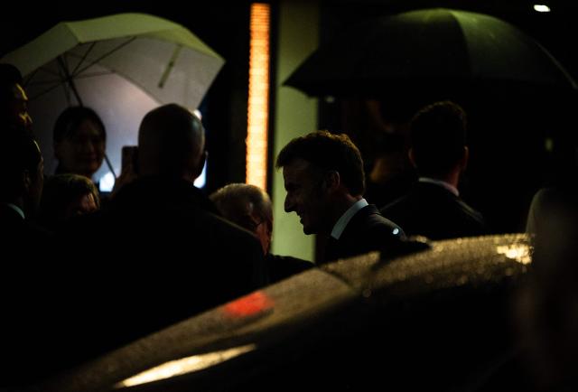 French President Emmanuel Macron (C) speaks with people on the street as he leaves the Ginza Motoji showroom on a rainy night in Tokyo on March 31, 2026. (Photo by ANDREW CABALLERO-REYNOLDS / AFP)