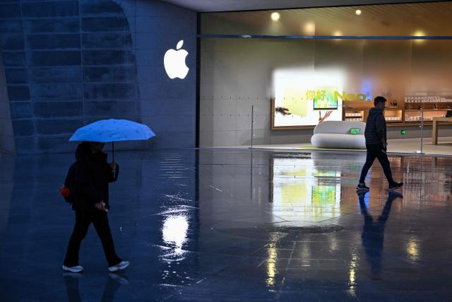 People walk past an Apple store in Jing'an district in Shanghai on March 31, 2026. (Photo by HECTOR RETAMAL / AFP)