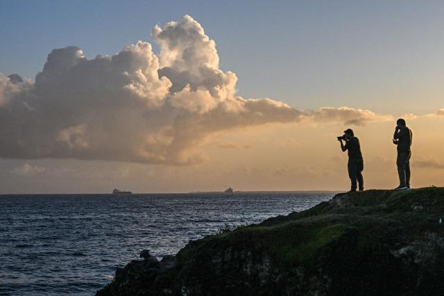 A man takes a picture of the Russian oil tanker Anatoly Kolodkin at the oil terminal in the port of Matanzas, northwestern Cuba, on March 31, 2026. The Anatoly Kolodkin, a tanker under US sanctions carrying 730,000 barrels of crude, is set to deliver the first crude shipment to Cuba since January after Washington gave the crisis-hit island a reprieve from an effective fuel blockade. (Photo by Yamil LAGE / AFP)