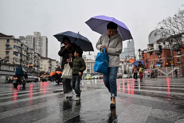 People walk across a road amid rainfall in Jing'an district in Shanghai on March 31, 2026. (Photo by HECTOR RETAMAL / AFP)