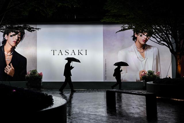 People walk past an advertisement for the luxury jeweler TASAKI in Jing'an district in Shanghai on March 31, 2026. (Photo by HECTOR RETAMAL / AFP)