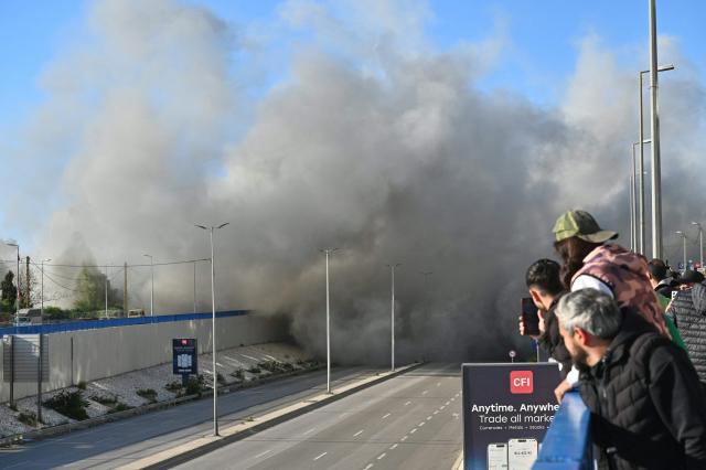 People watch smoke rising from the site of an Israeli strike that targeted a building adjacent to the highway that leads to Beirut's international airport on March 31, 2026. A strike hit a building adjacent to Beirut's main airport road on March 31, AFPTV's live broadcast showed, after the Israeli military warned it would hit a "Hezbollah facility". Lebanon was pulled into the Middle East conflict when Tehran-backed armed group Hezbollah fired rockets at Israel on March 2 in revenge for the killing of Iran's supreme leader, the opening salvo in the US-Israeli war against the Islamic republic. (Photo by FADEL itani / AFP) / 
