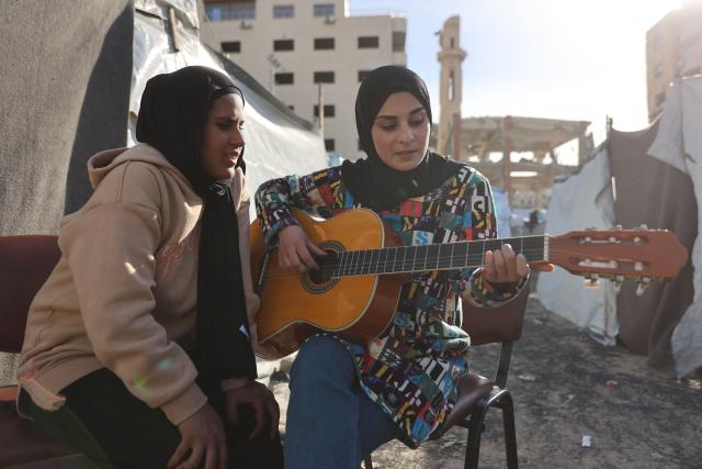 Rula Daloul, 32, from Zeitoun neighborhood, teaches a displaced Palestinian child along with others music and singing among tents at a shelter in Gaza City on March 31, 2016. Violence has persisted in Gaza despite a ceasefire which came into effect on October 10, with both Israel and Hamas regularly accusing each other of violations. (Photo by Omar AL-QATTAA / AFP)