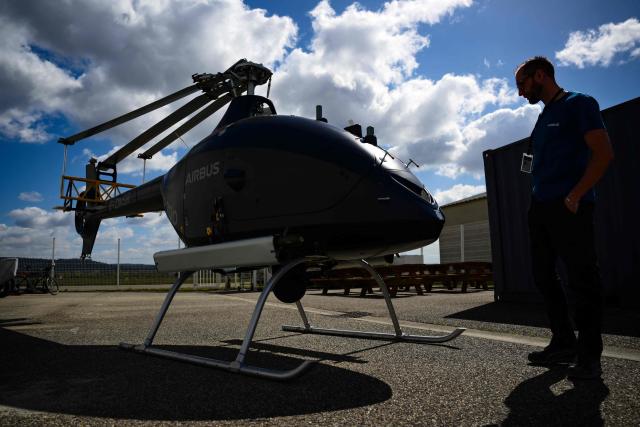 An employee inspects an Airbus VSR700 uncrewed aerial system (UAS) helicopter drone at the Survey Copter factory, an Airbus subsidiary in Pierrelatte, southern France on March 31, 2026. At Survey Copter, a French SME integrated into Airbus, the European aerospace corporation is leaning on its know-how in helicopters to develop drones — which have become the sinews of modern warfare — and to make them cooperate with manned aircraft. (Photo by OLIVIER CHASSIGNOLE / AFP)