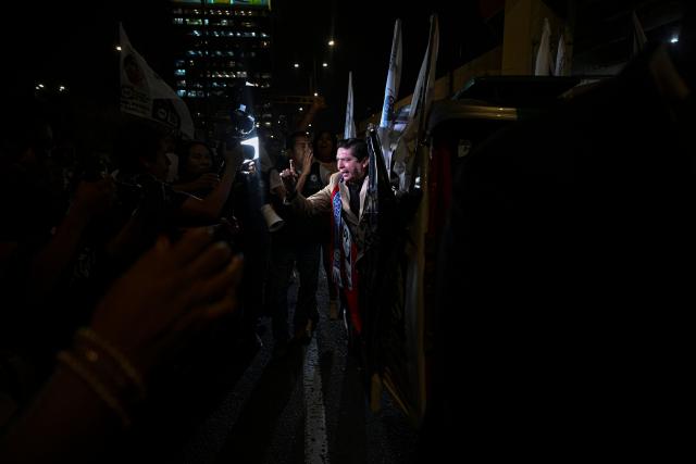 Peru's presidential candidate Herbert Caller, for the Patriotic Party of Peru, waves from a "tuktuk" upon his arrival for the second round of debates on education and employment at the Lima Convention Center in Lima on March 31, 2026. Peru will hold presidential elections on April 12. (Photo by ERNESTO BENAVIDES / AFP)