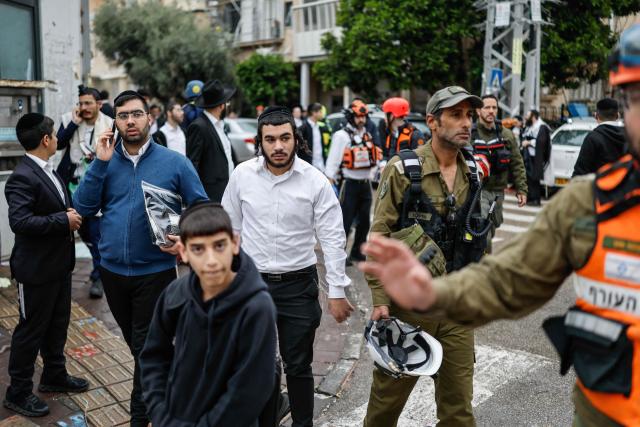A man looks on as first responders work at the scene of an impact following an Iranian strike over Bnei Brak in central Israel on April 1, 2026. The Israeli military said its air defences responded to a missile attack from Iran on April 1, with warning sirens activated across central Israel. (Photo by Marco Longari / AFP) / 