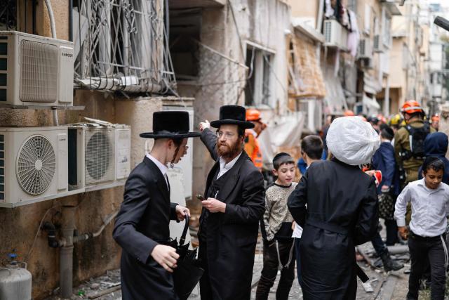 Ultra-Orthodox Jews and first responders stand at the scene of an impact following an Iranian strike over Bnei Brak in central Israel on April 1, 2026. The Israeli military said its air defences responded to a missile attack from Iran on April 1, with warning sirens activated across central Israel. (Photo by Marco Longari / AFP) / 
