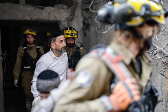 A man walking alongside first responders surveys the damage at the scene of an impact following an Iranian strike over Bnei Brak in central Israel on April 1, 2026. The Israeli military said its air defences responded to a missile attack from Iran on April 1, with warning sirens activated across central Israel. (Photo by Marco Longari / AFP) / 