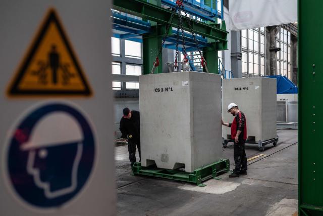 (FILES) Two workers stand next to the automated storage bridge in Montchanin, eastern France, on February 28, 2024, that will be used to transport nuclear waste to the CIGEO site (centre industriel de stockage géologique) « industrial geological disposal center » in Bure, eastern France. The cost of Cigeo, a project to bury the most radioactive nuclear waste in Bure (Meuse), has been estimated by the state at 33.36 billion euros, up from the 25 billion envisaged in 2016, according to a decree published on April 1, 2026 in the Journal officiel. This updated total cost, based on January 2025 economic conditions, falls within the range estimated in May 2025 by the National Agency for Radioactive Waste Management (Andra), the project's developer, which stood between 26.1 and 37.5 billion euros. (Photo by ARNAUD FINISTRE / AFP)