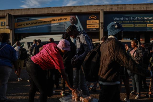 A street vendor sells homemade cookies to  commuters queueing to board a minibus taxi at Bara Taxi rank in Soweto on April 1, 2026, a day after South Africa lowered its fuel tax for a month to offset a global oil price surge driven by the Iran war, even as pump prices rose in one of the steepest increases on record. (Photo by Phill Magakoe / AFP)