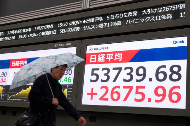 A woman walks past an electronic quotation board displaying the closing numbers of the Nikkei Stock Average on the Tokyo Stock Exchange along a street in Tokyo on April 1, 2026. (Photo by Kazuhiro NOGI / AFP)