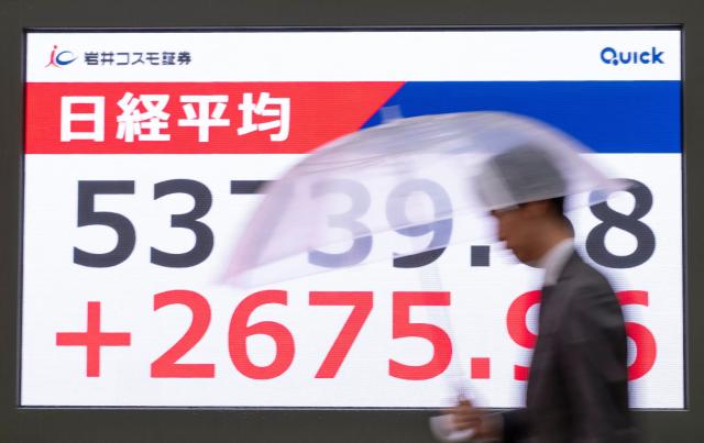 A man walks past an electronic quotation board displaying the closing numbers of the Nikkei Stock Average on the Tokyo Stock Exchange along a street in Tokyo on April 1, 2026. (Photo by Kazuhiro NOGI / AFP)