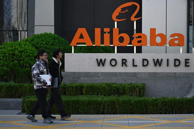 Employees walk past a company logo during a tour at the Alibaba office in Beijing on April 1, 2026. (Photo by WANG Zhao / AFP)