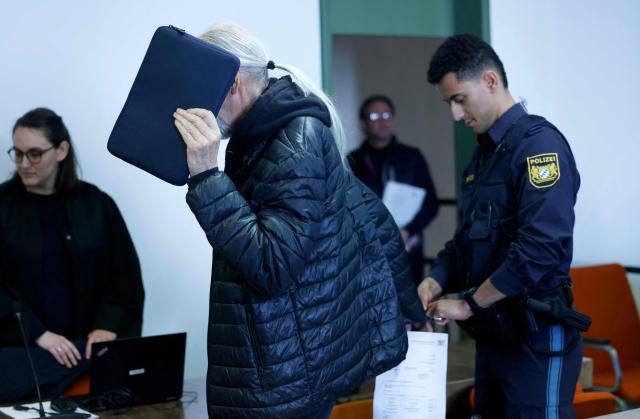 Defendant 71-year-old Joachim K (C) hides his face as he is brought to the courtroom prior to the start of a trial against him and two others for backing the self-styled "United Patriots" group, part of Germany's extremist Reichsbuerger scene, on April 1, 2026 at the higher Regional court of Munich, southern Germany. The group, referred to by investigators as the Kaiserreichsgruppe or "Imperial Group", was allegedly committed to forcibly establishing a new authoritarian Germany based on the old 1871 Imperial Constitution. (Photo by Michaela Stache / AFP) / GERMAN COURT REQUESTS THAT THE FACE OF THE DEFENDANT MUST BE MADE UNRECOGNISABLE