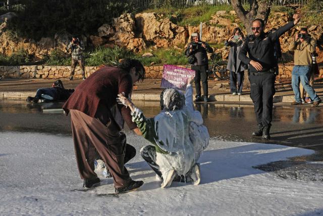 Veteran photographer and former AFP employee Menahem Kahana (top left) lies on the ground next to a protester who was sprayed with water mixed with a white liquid during a demonstration against a death penalty bill passed by Israel's parliament, outside the parliament in Jerusalem on March 31, 2026. An international media association on March 31, condemned what it described as a "violent and unprovoked attack" on Kahana. According to the Foreign Press Association, which represents hundreds of journalists in Israel and the Palestinian territories, Kahana was "sprayed at a close distance by a water cannon" at the protest outside the Knesset. (Photo by AHMAD GHARABLI / AFP)