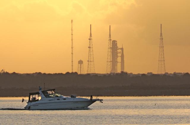 A boat moves along the Indian River as NASA's Artemis II Space Launch System (SLS) is seen in the distance at the Kennedy Space Center at sunrise in Cape Canaveral, Florida on April 1, 2026. The first window to launch from the Kennedy Space Center in Florida opens Wednesday, April 1 at 6:24 pm (22:24 GMT), and NASA officials said the countdown began at 4:44 pm. (Photo by Gregg Newton / AFP)
