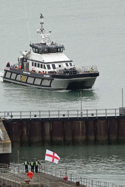 CORRECTION / A man waves a St George's cross England flag as a British Border Force vessel carrying migrants picked up at sea, while attempting to cross the English Channel from France, arrives into the Port of Dover in southeast England, on April 01, 2026.  (Photo by JUSTIN TALLIS / AFP) / “The erroneous mention[s] appearing in the metadata of this photo by JUSTIN TALLIS has been modified in AFP systems in the following manner: The location should read [Dover, Kent, Unitd Kingdom] instead of [Dover, Delaware, USA]. Please immediately remove the erroneous mention[s] from all your online services and delete it (them) from your servers. If you have been authorized by AFP to distribute it (them) to third parties, please ensure that the same actions are carried out by them. Failure to promptly comply with these instructions will entail liability on your part for any continued or post notification usage. Therefore we thank you very much for all your attention and prompt action. We are sorry for the inconvenience this notification may cause and remain at your disposal for any further information you may require.”