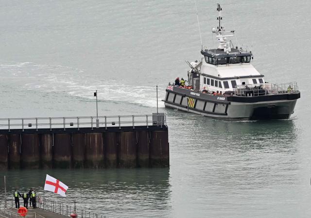 CORRECTION / A man waves a St George's cross England flag as a British Border Force vessel carrying migrants picked up at sea, while attempting to cross the English Channel from France, arrives into the Port of Dover in southeast England, on April 01, 2026.  (Photo by JUSTIN TALLIS / AFP) / “The erroneous mention[s] appearing in the metadata of this photo by JUSTIN TALLIS has been modified in AFP systems in the following manner: The location should read [Dover, Kent, Unitd Kingdom] instead of [Dover, Delaware, USA]. Please immediately remove the erroneous mention[s] from all your online services and delete it (them) from your servers. If you have been authorized by AFP to distribute it (them) to third parties, please ensure that the same actions are carried out by them. Failure to promptly comply with these instructions will entail liability on your part for any continued or post notification usage. Therefore we thank you very much for all your attention and prompt action. We are sorry for the inconvenience this notification may cause and remain at your disposal for any further information you may require.”