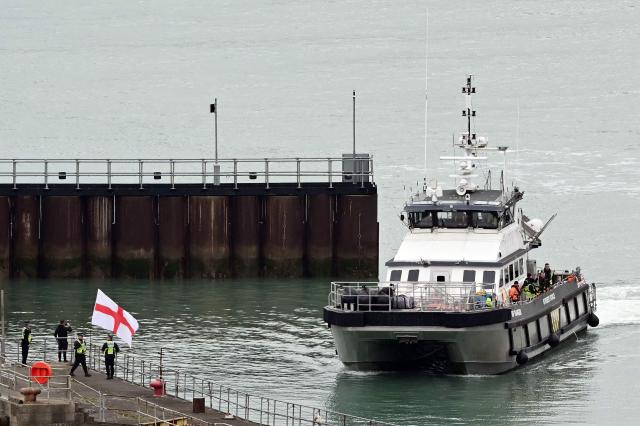 CORRECTION / A man waves a St George's cross England flag as a British Border Force vessel carrying migrants picked up at sea, while attempting to cross the English Channel from France, arrives into the Port of Dover in southeast England, on April 01, 2026.  (Photo by JUSTIN TALLIS / AFP) / “The erroneous mention[s] appearing in the metadata of this photo by JUSTIN TALLIS has been modified in AFP systems in the following manner: The location should read [Dover, Kent, Unitd Kingdom] instead of [Dover, Delaware, USA]. Please immediately remove the erroneous mention[s] from all your online services and delete it (them) from your servers. If you have been authorized by AFP to distribute it (them) to third parties, please ensure that the same actions are carried out by them. Failure to promptly comply with these instructions will entail liability on your part for any continued or post notification usage. Therefore we thank you very much for all your attention and prompt action. We are sorry for the inconvenience this notification may cause and remain at your disposal for any further information you may require.”
