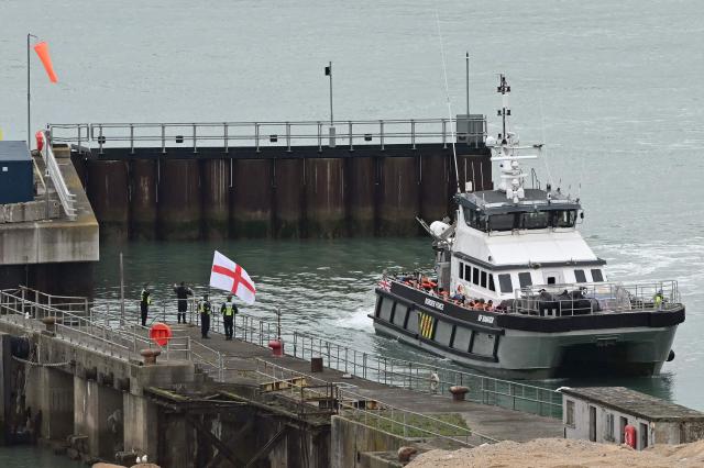 CORRECTION / A man waves a St George's cross England flag as a British Border Force vessel carrying migrants picked up at sea, while attempting to cross the English Channel from France, arrives into the Port of Dover in southeast England, on April 01, 2026.  (Photo by JUSTIN TALLIS / AFP) / “The erroneous mention[s] appearing in the metadata of this photo by JUSTIN TALLIS has been modified in AFP systems in the following manner: The location should read [Dover, Kent, Unitd Kingdom] instead of [Dover, Delaware, USA]. Please immediately remove the erroneous mention[s] from all your online services and delete it (them) from your servers. If you have been authorized by AFP to distribute it (them) to third parties, please ensure that the same actions are carried out by them. Failure to promptly comply with these instructions will entail liability on your part for any continued or post notification usage. Therefore we thank you very much for all your attention and prompt action. We are sorry for the inconvenience this notification may cause and remain at your disposal for any further information you may require.”